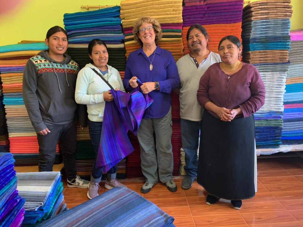 Owner Amy Johnstone with her friends and weavers in Ecuador in front of a stack of alpaca blankets